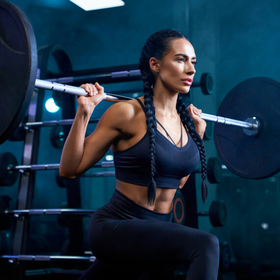 woman with dark hair in braids lifting a barbell in a gym